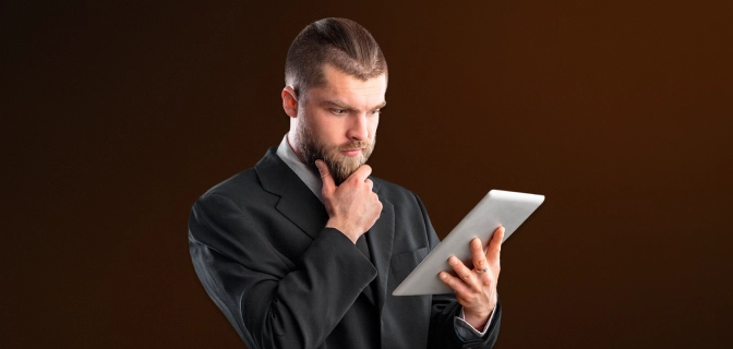 imagem mostra homem com a mão no queixo enquanto olha atentamente para o tablet que segura em sua outra mão.