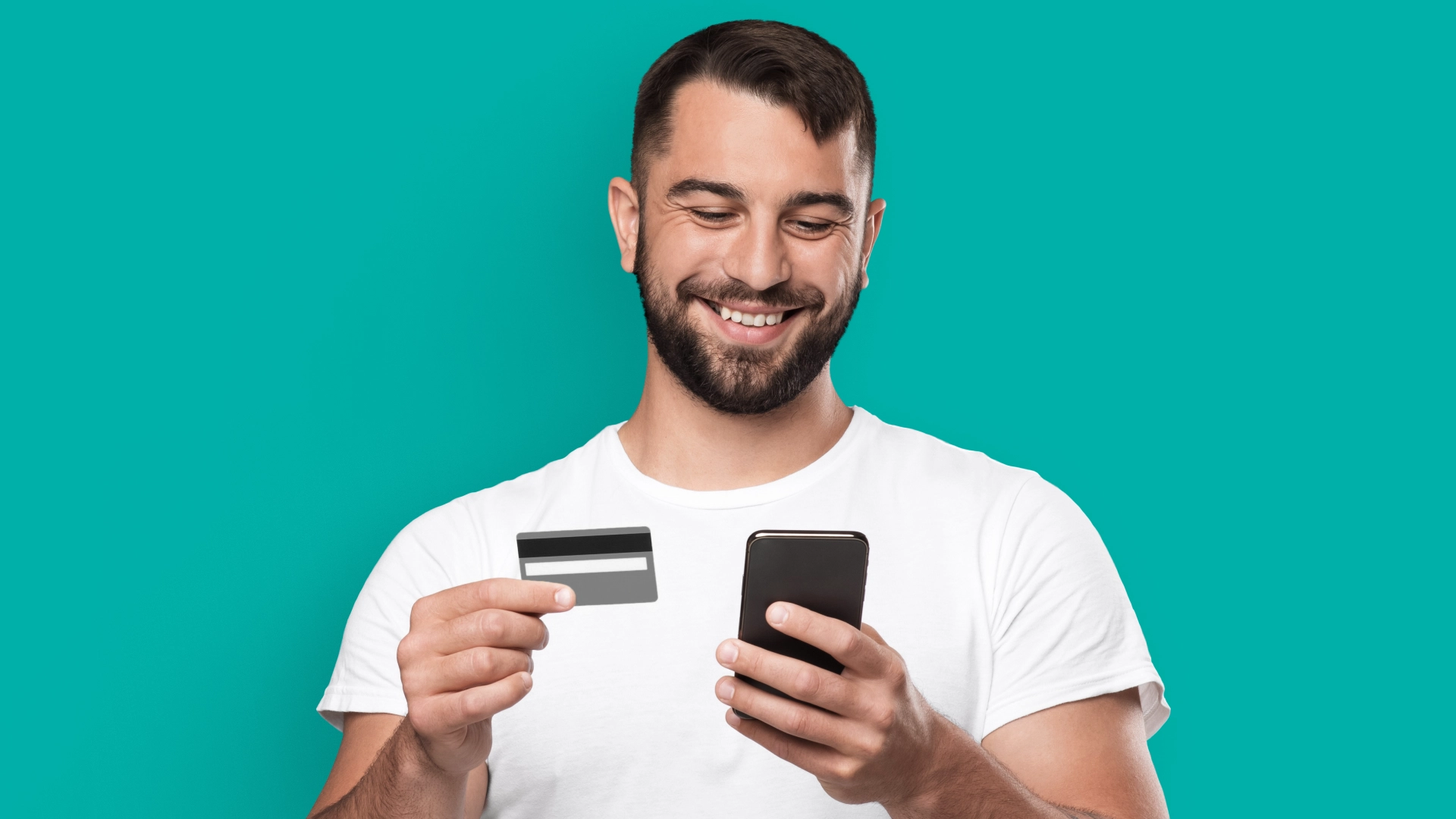 Imagem mostra homem sorrindo ao utilizar um celular e um cartão de débito