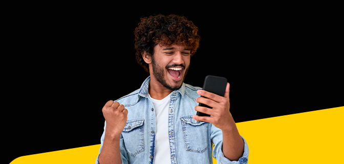 imagem mostra homem de jaqueta jeans sorrindo, com expressão de comemoração, enquanto segura um smartphone.