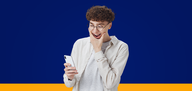 Imagem mostra um homem sorrindo surpreso ao olhar para o smartphone que segura em sua mão.
