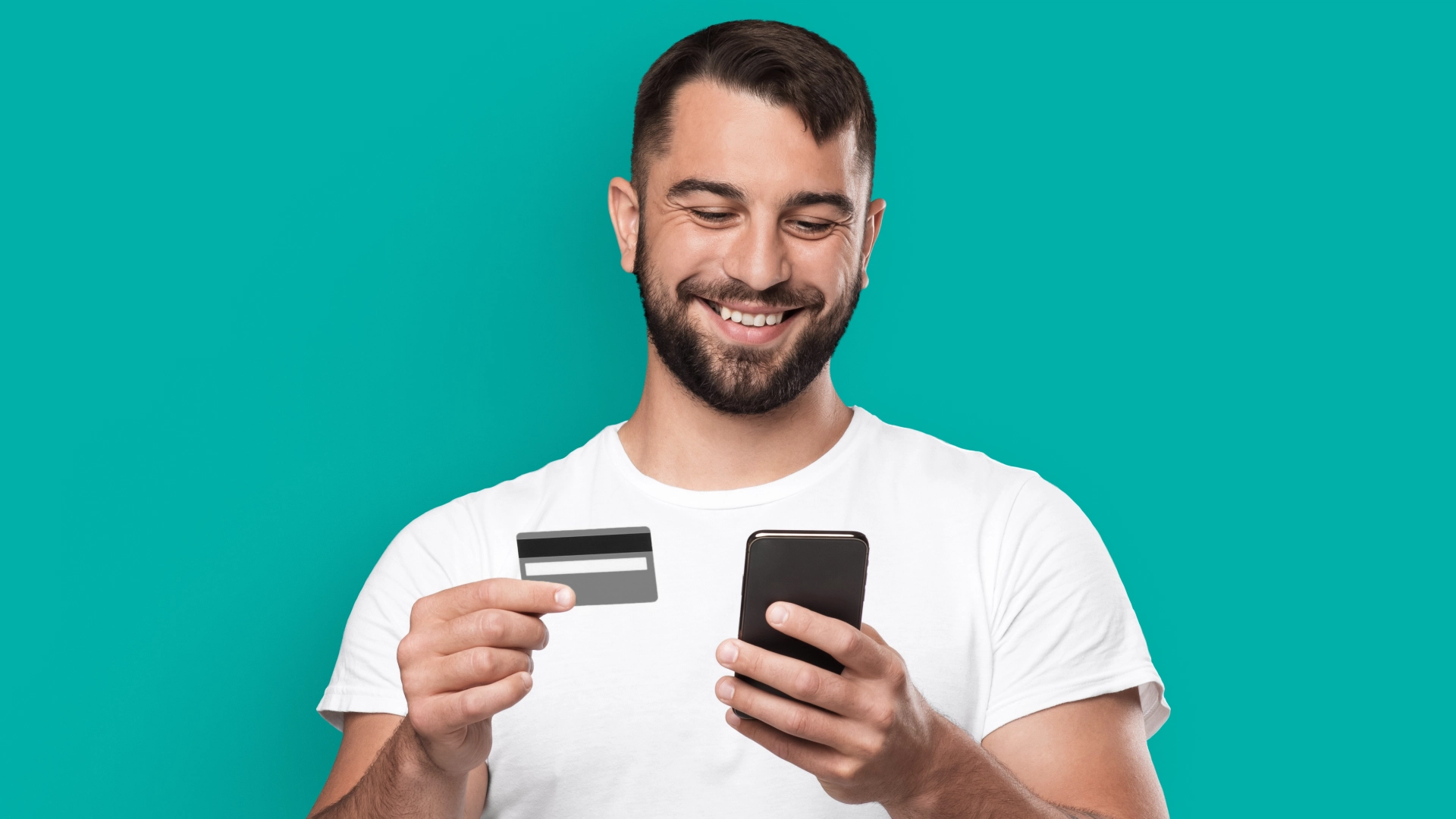 Imagem mostra homem sorrindo e segurando um cartão de débito e um celular